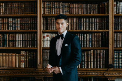Slim fit classic black dinner suit in light weight, 100% wool. 3 piece dinner suit with traditional black tux jacket, classic black dinner suit trousers and black horseshoe waistcoat. Features a slim fit 1 button black dinner jacket with classic black satin peak lapel. Worn with white studded dress shirt with French cuff shirt and large tom ford style bow tie and white pocket square.